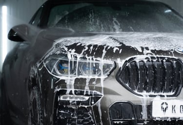 front grill, lights and bumper of a grey bmw that is  dripping wet with soap running down. 