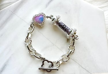 Features a silver chain with larger, oval links. It has a central cylindrical element with a dark pa