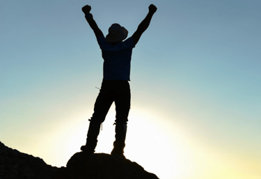 Silhouetted figure arms raised in success on peak