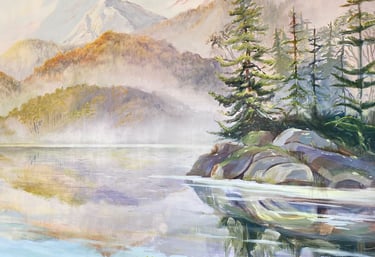 A forested island in front of foggy mountains reaching down to the shore.