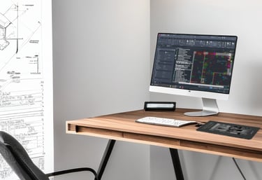 Stanowisko pracy z rysunkiem technicznym w tle oraz komputerem z AutoCADem