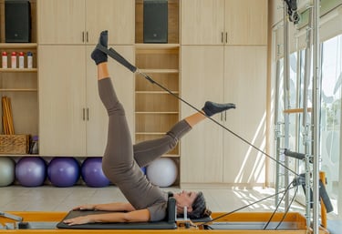 Woman lying on a Pilates Reformer doing a leg exercise using the foot straps in the Cabo San Lucas studio.
