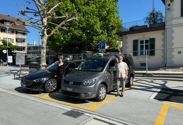Zwei Taxiautos. Ein grauer VW Caddy und ein schwarzer Mercedes E-Klasse samt Taxifahrer