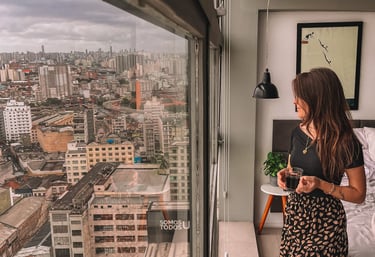 Uma pessoa em pé com uma xícara de café nas mãos, enquanto avista a cidade de São Paulo do topo.