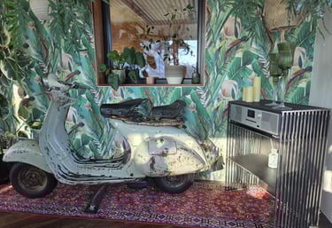Vintage-Vespa als dekoratives Highlight vor Dschungel-Tapete neben modernem Holz-Sideboard.