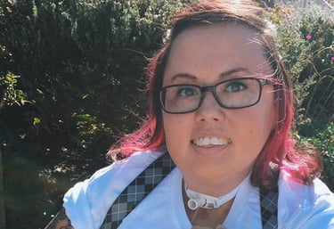 Photo of Stacey with suspenders, pink hair, tee shirt that says "Famous witches", with tattoos showing.