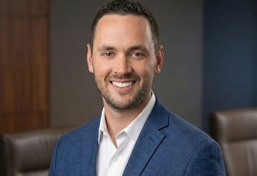 Professional headshot of a smiling male executive in a blue blazer and white shirt in an office setting.