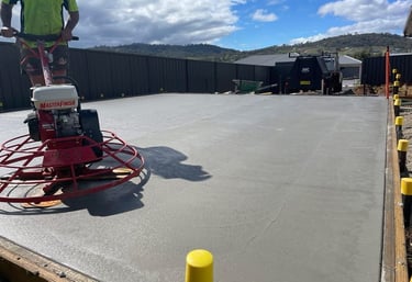 Professional concreter using a power trowel machine to finish a fresh concrete slab for a backyard patio.