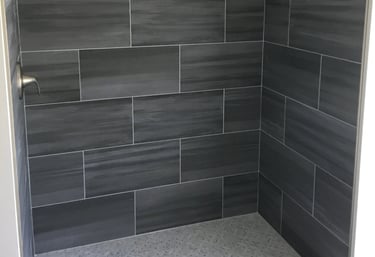 Walk-in shower with dark gray wall tiles, light gray mosaic floor, and stainless steel fixtures