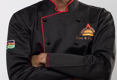 A smiling young chef wearing a professional black double-breasted culinary jacket with red trim.