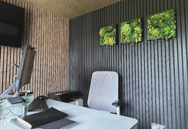 Modern home office featuring wood slat wall panels, a white desk, and framed artificial succulent wall art.