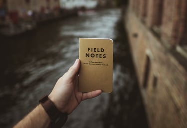 Journal titled "Field Notes" held up in front of a Canal; Photo by Vadim Sadovski on Unsplash 