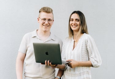 Raphael und Vanessa Bogner stehen vor einer weißen Wand mit einem Macbook in der Hand