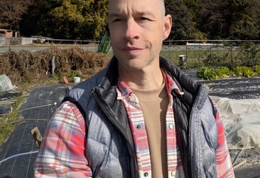 a man in a plaid shirt and vest jacket standing in a garden area