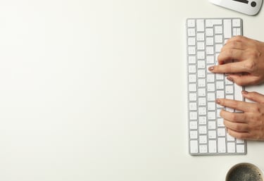 Mains de professionnelle tapant sur un clavier Apple blanc — rédaction de contenu stratégique et communication numérique