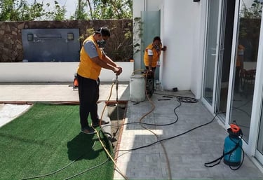 Professional pest control technicians in yellow vests applying termite treatment to a residential patio.