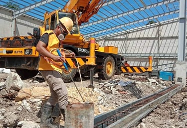 A construction worker in safety gear works near a Kato crane at an industrial building site.