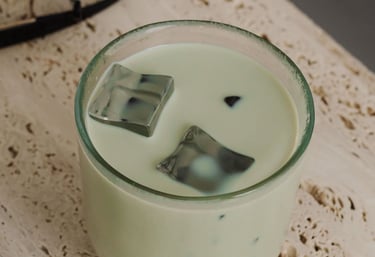 Iced matcha green tea latte with large ice cubes in a glass on a travertine stone surface.