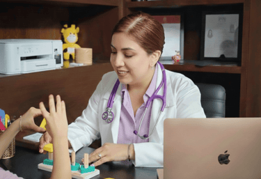 Dra Isis Pediatra con bata blanca utilizando bloques de madera durante una evaluación de un niño