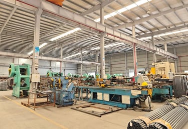 Industrial metal display racks workshop with heavy machinery and bundles of steel pipes.