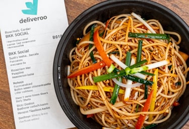 A cozy dining table with a laptop open on the Deliveroo app showing available meals.