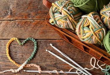 Corazón tejido a crochet rodeado de ovillos de algodón de colores y ganchos de crochet