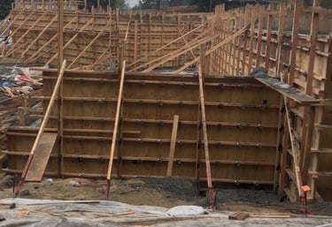 Wooden concrete formwork for a retaining wall foundation at a residential construction site.