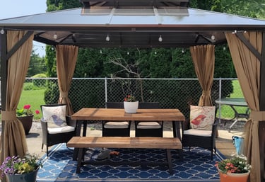 Hardtop backyard gazebo with outdoor dining table, benches, and privacy curtains on a patio rug.