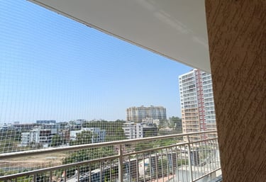 A bright balcony secured with a neatly installed white safety net overlooking a cityscape.