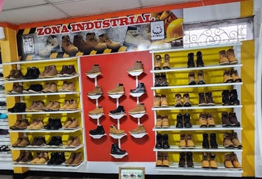 Botas de seguridad y calzado industrial de alta resistencia exhibidos en estantes blancos.