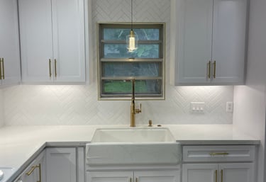 Modern white kitchen remodel with shaker cabinets, gold hardware, and a white farmhouse sink.
