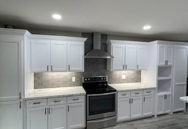 Modern white kitchen cabinets with marble countertops and a gray subway tile backsplash.