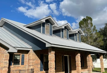 Modern suburban home with red brick exterior, blue siding, and a durable grey metal roof under a blue sky.