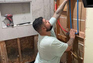 A plumber installing blue and red PEX piping for a shower during a bathroom renovation project.
