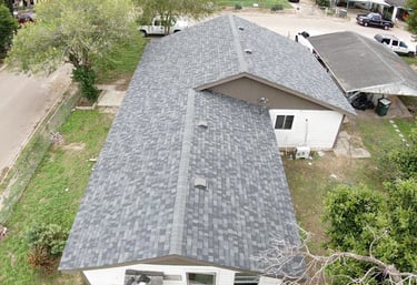 Aerial view of a residential home with newly installed grey architectural asphalt shingles on a gabled roof.