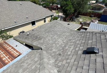 Elevated view of a residential roof featuring gray asphalt shingles and a roof vent in a suburban neighborhood.