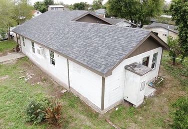 Aerial view of a suburban home featuring new grey asphalt roof shingles and white siding.