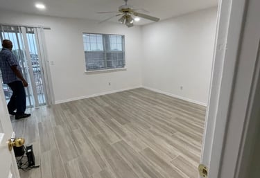 Empty modern living room featuring light wood-look tile flooring, white walls, and a ceiling fan with lights.