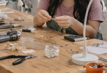 Un joyera utiliza alicates y herramientas en una mesa de madera para crear accesorios artesanales