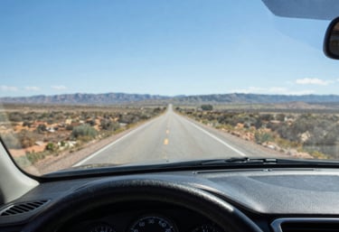 Detailed shot of a car dashboard viewed through a flawlessly installed, crystal-clear windshield. The North American / US landscape ahead is sharp, under a bright sky blue atmosphere.