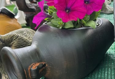 Vibrant magenta petunias blooming inside a rustic black ceramic vase at an outdoor pottery market.