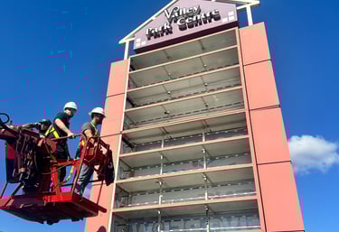 Technicians in a lift bucket performing maintenance on a tall commercial pylon sign at Valley Park Centre.