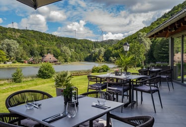 Außenterrasse eines Restaurants mit Blick auf See, grüne Hügel und Windkraftanlagen