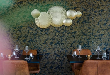 Elegant gedeckte Restauranttische mit Weingläsern vor gold-schwarzer Blumentapete
