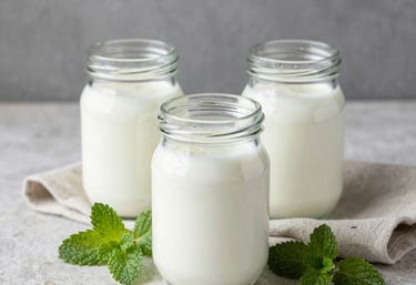 Still life with glass jars of fresh kefir, green mint leaves, and a linen napkin on a light stone surface, minimalist and clean aesthetic.