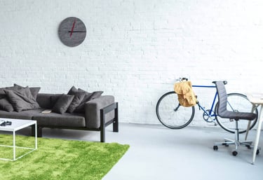 Modern studio apartment with a grey sofa, green shag rug, and blue bicycle against a white brick wall.
