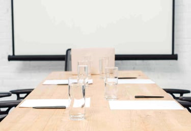 Empty corporate meeting room with water glasses, pens, and paper on a wooden table before a presentation.
