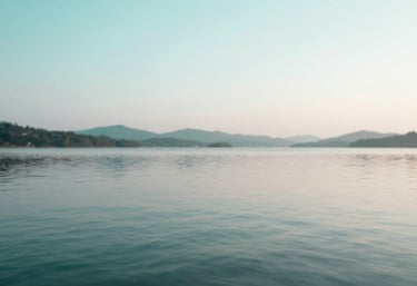 A peaceful landscape with calm waters reflecting a soft sky, utilizing the brand palette of #A7D9D3 and #F8FBFB. Represents mental clarity.