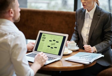 Two business professionals reviewing an SEO strategy flowchart on a laptop in a cafe setting.
