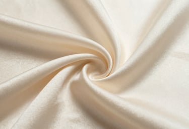 A close-up shot of shimmering soft cream silk fabric. The lighting emphasizes the delicate fibers and the premium, reflective quality of the material.